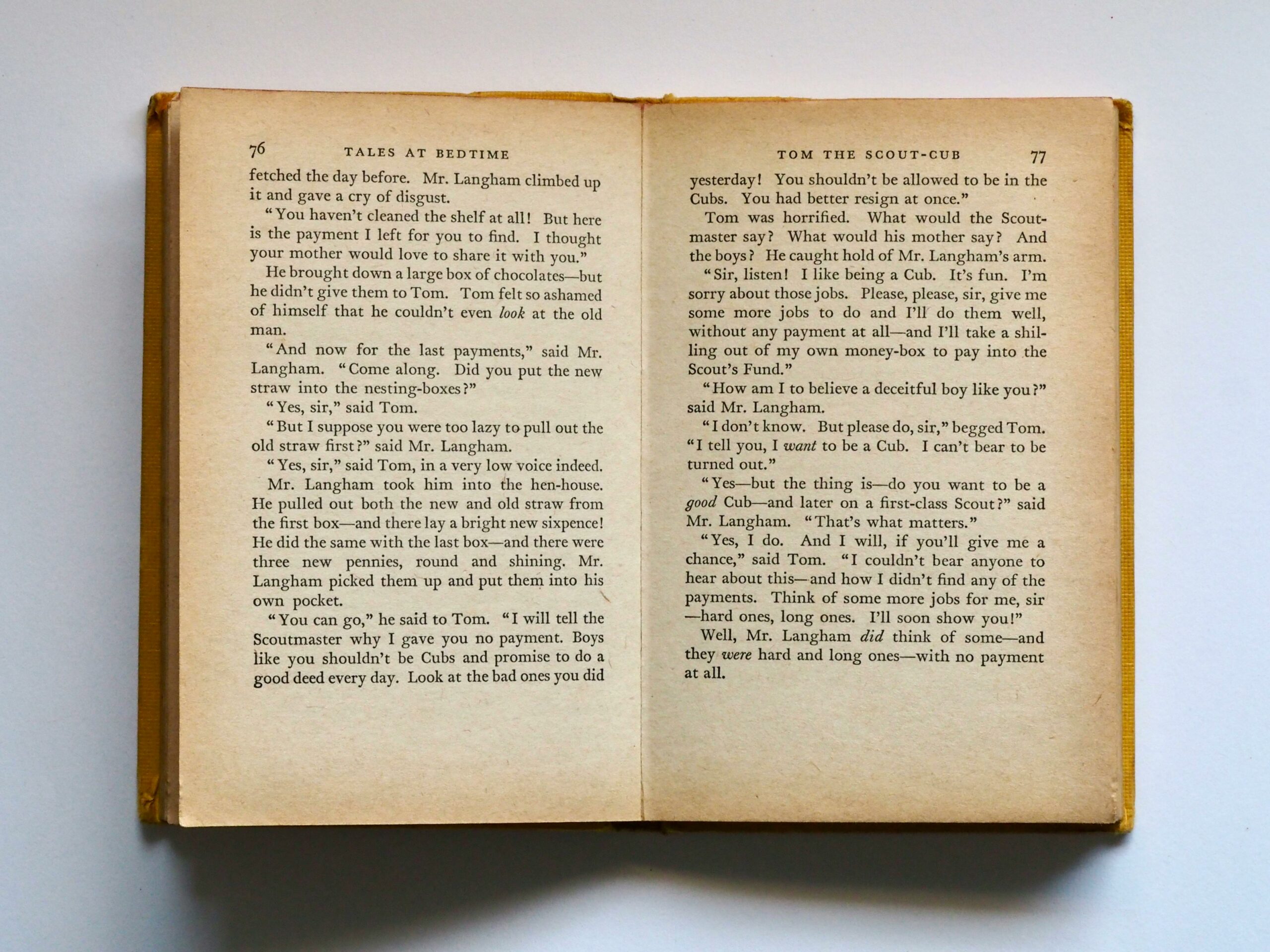 Vintage book opened to pages 76-77, displaying classic literature text in soft lighting.